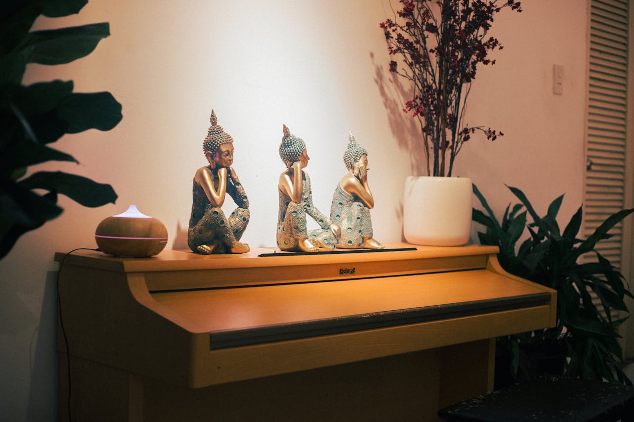 Tranquil indoor scene with Buddha statues on a piano, surrounded by plants and decor.