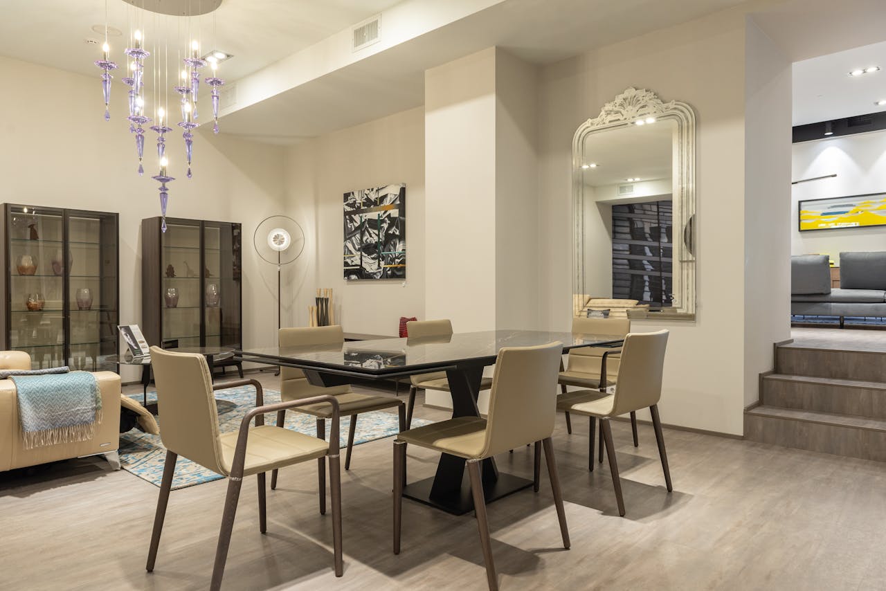 Sophisticated dining room featuring a modern glass top table, beige chairs, and a stylish chandelier.